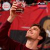 A man proudly lifts an Ottawa Senators collector whiskey glass above his head with a bright smile and crowd behind him!