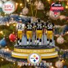 Holiday ornament with four Steelers legends in black and gold uniforms, snowy overlay and glowing lights in a festive setting.