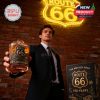 Man in formalwear holding up Route 66 100th anniversary whiskey glass near neon sign and collector’s box!