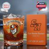 A whiskey glass with the Sam Houston Bearkats logo and musical motif stands on a table at a football stadium. The glass contains a drink with ice, and a matching gift box highlights the SH branding and team slogan!