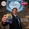 Man holding up a San Diego FC whiskey glass with ice and golden liquid in front of a glowing club logo!