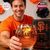 A joyful fan at a party holds out the San Francisco Giants 142nd anniversary whiskey glass, surrounded by themed decorations and the team's celebratory display.