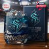 Seattle Kraken anniversary whiskey glass with blue drink and ice cubes placed on a wooden surface with a branded gift box and hockey arena background.