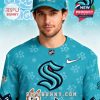 Display of Bluey x NHL Kraken fan gear showing full jersey front and back plus a hat, in bright teal with paw prints and cartoon hockey details!