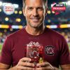 A fan wearing Gamecocks apparel proudly displays a branded anniversary whiskey glass in a sports venue setting.
