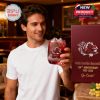A relaxed fan in a lounge holds and examines a celebratory Gamecocks whiskey glass beside its commemorative packaging.