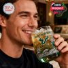 Man smiling while drinking from a South Florida Bulls whiskey glass with ice and golden liquid featuring the Bulls logo and tropical design elements in a warm indoor environment!