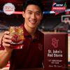 A cheerful young man showcasing a branded whiskey glass commemorating St. John’s Red Storm anniversary while posing courtside in a stadium environment!