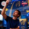 A man in a sports bar holds up a St. Louis City SC whiskey glass to admire its design under glowing lights.