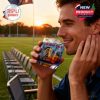 A man by the soccer field smiles while drinking from the St. Louis City SC whiskey glass during golden hour.