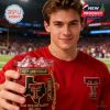 A smiling young fan holds a Texas Tech Red Raiders 100th Anniversary whiskey glass with gold text and logos at a sports stadium!