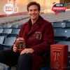A fan wearing a maroon coat sits in stadium seats holding the Texas Tech 100th Anniversary whiskey glass, next to its decorative box!