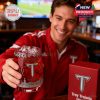 A fan in red extends a Troy Trojans whiskey glass toward the viewer in a warm bar environment!
