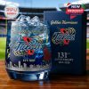 A Tulsa Golden Hurricane 131st anniversary whiskey glass and its matching gift box rest on a wooden surface with a baseball stadium in the background!