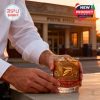 Close-up of a man's hands holding the USPS 250th Anniversary whiskey glass at sunset outside a traditional post office, evoking a sense of pride and nostalgia.