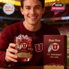 Smiling Utah Utes fan holding a red anniversary whiskey glass with matching box inside a football stadium!