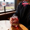 Man holding Utah Utes anniversary whiskey glass with ice while seated near a stadium window!
