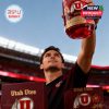 Fan raising Utah Utes anniversary whiskey glass proudly under stadium lights with cheering crowd!