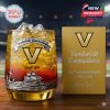A golden Vanderbilt Commodores whiskey glass sits beside a matching gold gift box, both commemorating the team's 136th anniversary with nautical motifs and vibrant sunset-inspired gradients.