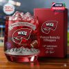 Commemorative WKU whiskey glass with red drink and ice on a wooden surface, placed next to a red box marked with the team’s logo and anniversary details against a stadium backdrop!