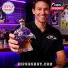 A person holding a Baltimore Ravens whiskey bottle with a crown top in a bar, with purple lighting in the background.