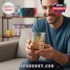 A man sitting in front of a game shelf holding a Pokémon glass with golden Eevee artwork and smiling warmly!