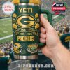 Excited fan in Packers jersey holding YETI anniversary mug at stadium.
