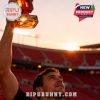 Man holding red university logo perfume bottle high with stadium and sunset behind!