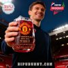Close-up of a man lifting the Manchester United anniversary glass in the air at the stadium, glowing red and gold with ice inside.