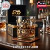 Whiskey glass with golden Star Wars designs on a coaster, elegant box behind it, surrounded by bar accessories in a dimly lit premium setting!