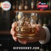 Close-up of hand holding a golden Star Wars 50th Anniversary glass with iconic etched designs, background softly lit with bar ambiance!
