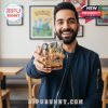 A smiling man in a café shows off a golden Pokémon whiskey glass surrounded by nostalgic wall art!