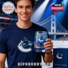 Man in dark blue Vancouver Canucks shirt holds a blue-tinted whiskey glass with detailed engravings celebrating the team's 56th anniversary.