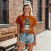 Rust orange tee with messy bun woman graphic, floral bandana, glasses, winking eye! Text 'LONGHORNS girl' in patterned font!