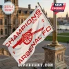 White Arsenal FC flag with red cannon logo and Champions 25/26 text flying on a metal pole outside a stone building!