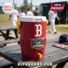A red water cooler sits on a wooden bench at a baseball field with players in the background!
