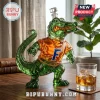 Green glass alligator decanter wearing an orange shirt with a blue letter F on a wooden table with a glass of whiskey!