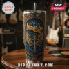 Judas Priest 2026 Faithkeepers tumbler with metallic gold cross wings and blue filigree background on a guitar shop table!