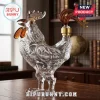 Clear glass rooster shaped liquor decanter with amber accents and gold stopper on a wooden table background!