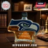 Glass whiskey bottle shaped like Seattle Seahawks logo with 1976-2026 50th Anniversary text on a dark wooden office desk!
