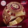 Gold Oklahoma Sooners 2026 NCAA baseball championship ring with red stones and clear diamond accents on velvet fabric.!