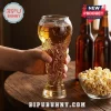 Hand holding a clear glass beer mug shaped like a world cup soccer trophy filled with amber ale on a wooden table.!