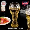 Clear glass beer mug shaped like the FIFA World Cup trophy filled with golden lager on a black background.!