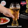 Hand holding a clear glass beer mug shaped like the FIFA World Cup trophy filled with golden lager against black background.!
