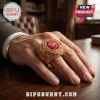 Gold-toned Arsenal FC championship ring with a red gemstone, engraved text, and club logo on a person's hand.!