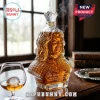 Clear glass bust-shaped whiskey decanter labeled The Queen's Reserve with a crown stopper on a wooden table.!