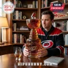 Man holding a glass whiskey decanter shaped like the Stanley Cup with Carolina Hurricanes branding on a wooden desk.!
