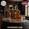 Letter B shaped glass whiskey decanter with black tiger stripes on a wooden barrel next to a crystal glass of amber liquor.!