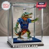 Faceted crystal alligator figurine in a blue jersey with 1906-2026 120th anniversary text inside a glass display case.!
