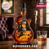 Electric guitar shaped glass whiskey bottle with Slash graphic, Jim Beam branding, and amber liquid on a wooden table.!